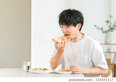 年輕的亞洲男子早餐吃烤麵包和沙拉。 135472117