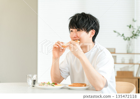 年輕的亞洲男子早餐吃烤麵包和沙拉。 135472118