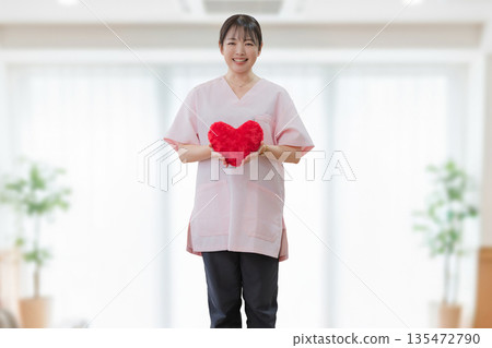 Smiling medical woman holding a heart Smiling medical woman holding a heart 135472790