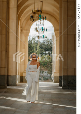Woman White Outfit Palace Archway - Fashionable woman walks through an archway in a white outfit in a palace. Woman White Outfit Palace Archway - Fashionable woman walks through an archway in a white outfit in a palace. 135473157