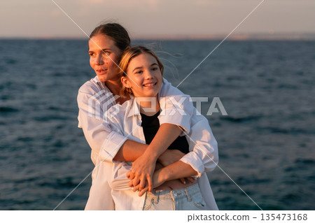 Mother Daughter Beach Sunset - Two women embrace while looking out at the ocean during a sunset. Mother Daughter Beach Sunset - Two women embrace while looking out at the ocean during a sunset. 135473168
