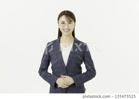 一位戴著眼鏡、西裝的年輕日本女性面帶微笑,雙手交叉放在白色背景上,看著鏡頭。 一位戴著眼鏡、西裝的年輕日本女性面帶微笑,雙手交叉放在白色背景上,看著鏡頭。 135473525