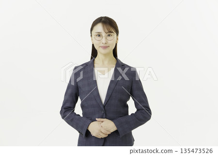 一位戴眼鏡的年輕日本女性穿著西裝，雙手交握，看向鏡頭，背景為白色。 135473526