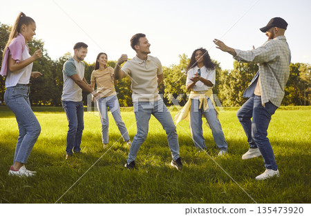 Sunny grassy park fun, diverse group of young people friends dancing, playing lively game, moving 135473920