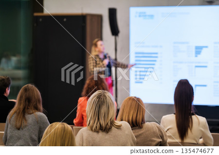 Business seminar with speaker presenting charts to attentive audience in modern conference room Business seminar with speaker presenting charts to attentive audience in modern conference room 135474677