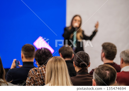 Speaker presenting to engaged audience at conference with blue and purple stage backdrop Speaker presenting to engaged audience at conference with blue and purple stage backdrop 135474694