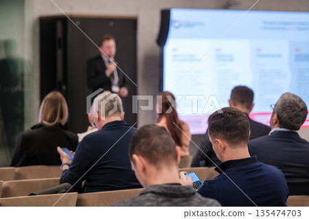 Business conference presentation in a modern seminar room with audience listening to a speaker 135474703