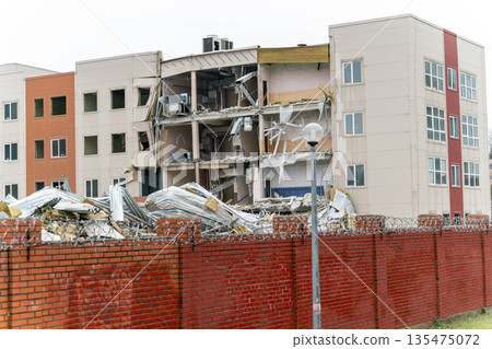 A partially demolished building with exposed walls and debris scattered around. A red brick fence surrounds the site, indicating construction or renovation work. 135475072