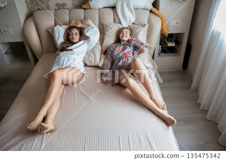 Women Bedroom Relaxation: Two women relax together on a bed in a bedroom, enjoying leisure time at home. Women Bedroom Relaxation: Two women relax together on a bed in a bedroom, enjoying leisure time at home. 135475342