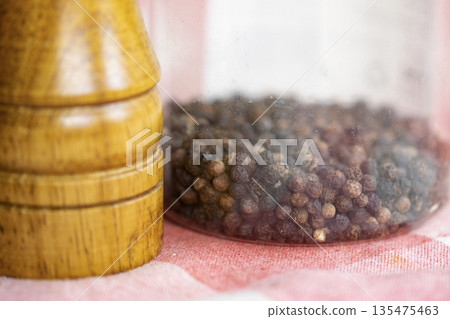 black peppercorns in a glass jar and wooden pepper mill 135475463