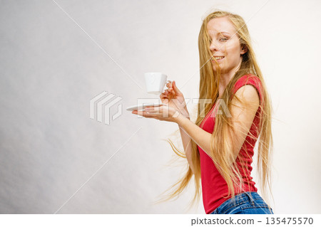 Blonde girl blowing hair holds coffee cup 135475570