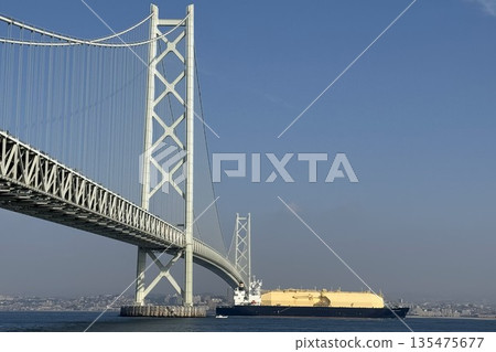 A distant view of a huge LNG gas carrier passing through the Akashi Kaikyo Bridge 135475677