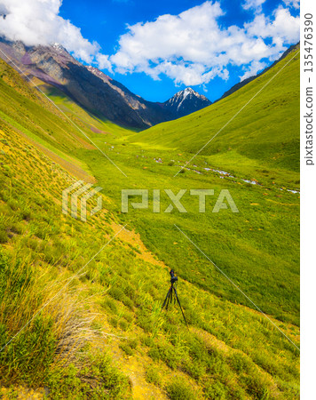 Camera on tripod in serene mountain valley during daytime 135476390
