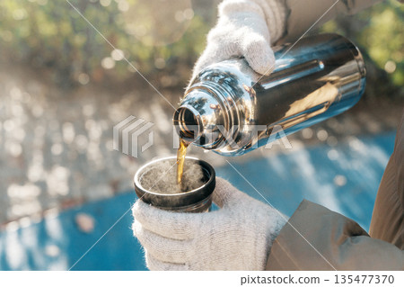 Coffee Pouring from Thermos into Cup on a Sunny Winter Day 135477370