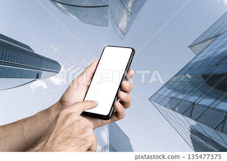 Smartphone Mockup in Hands Against Modern City Skyscrapers Smartphone Mockup in Hands Against Modern City Skyscrapers 135477375