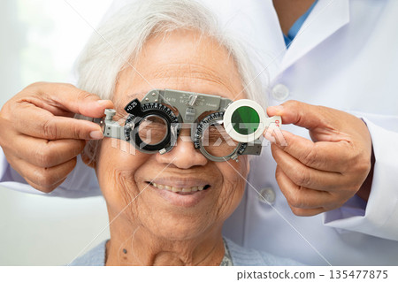 Asian senior woman wearing ophthalmic vision eye test and using optical trial frame. 135477875