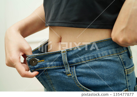 Young Asian woman losing weight wearing loose pants in oversize jeans. Young Asian woman losing weight wearing loose pants in oversize jeans. 135477877