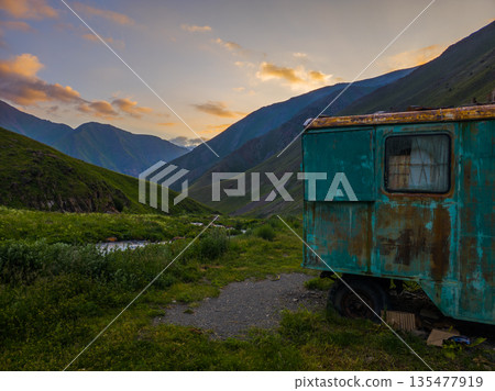 Rusty teal trailer by river in mountainous region at sunset Rusty teal trailer by river in mountainous region at sunset 135477919