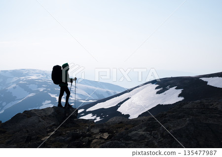Hiker with a backpack standing against the background of snowy spring mountains Hiker with a backpack standing against the background of snowy spring mountains 135477987