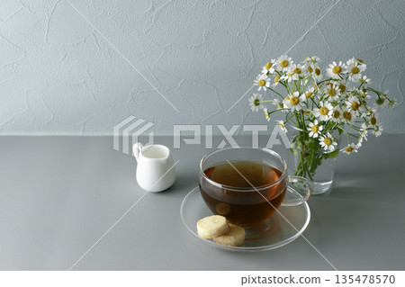 Tea and Matricaria: Still life of glass teacup and cookies. Copy space on blue-gray background. Tea and Matricaria: Still life of glass teacup and cookies. Copy space on blue-gray background. 135478570