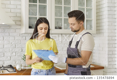 Man plumber signing contract with female client for plumbing services at home. 135478894