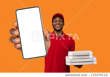 Fast Service And Best Food Delivery During Pandemic. Positive black courier wearing red uniform and cap holding pizza boxes from restaurant and showing okay sign gesture, isolated on orange background 135479118