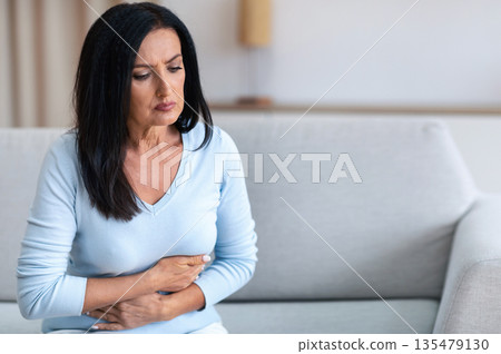 Food Poisoning. Mature Woman Suffering From Stomachache After Eating, Touching Aching Abdomen Sitting On Couch At Home. Health Problem, Appendicitis, Abdominal Inflammation And Gastritis Concept Food Poisoning. Mature Woman Suffering From Stomachache After Eating, Touching Aching Abdomen Sitting On Couch At Home. Health Problem, Appendicitis, Abdominal Inflammation And Gastritis Concept 135479130