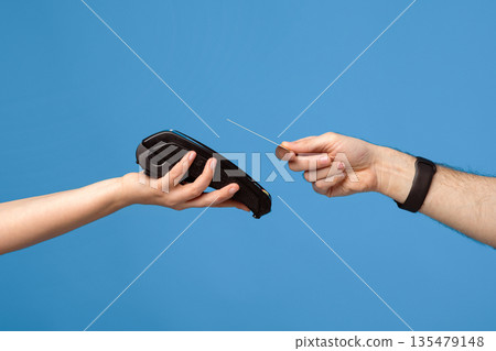 Unrecognizable male and female hands with credit card and money terminal over blue studio background. Young guy making contactless payment during coronavirus pandemic, closeup Unrecognizable male and female hands with credit card and money terminal over blue studio background. Young guy making contactless payment during coronavirus pandemic, closeup 135479148