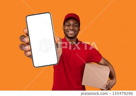 Smiling Bearded African American Delivery Man Showing Smartphone With Empty Black Screen Holding Cardboard Box Recommending Postal Express Shipping App Standing Isolated Over Yellow Studio Background 135479298