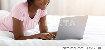 Online dating concept. Happy young black woman flirting in internet, typing on laptop in bed and smiling, copy space. Cheerful african american lady spending weekend at home, using laptop 135479309