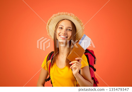 Smiling young woman tourist with backpack holding passport and flight tickets, yellow studio background. Cheerful lady backpacker ready to travel, looking at camera and smiling, copy space Smiling young woman tourist with backpack holding passport and flight tickets, yellow studio background. Cheerful lady backpacker ready to travel, looking at camera and smiling, copy space 135479347