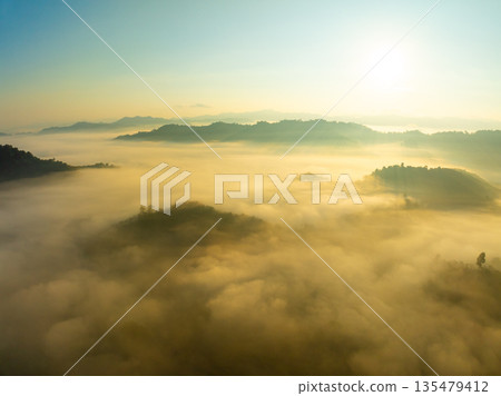 Aerial view of flowing fog waves on mountain tropical rainforest,Bird eye view image over the clouds Amazing nature background with clouds and mountain peaks in Thailand 135479412