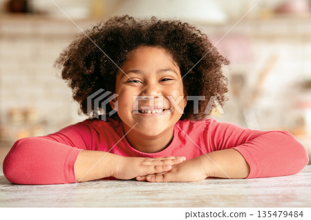 Happy Child. Closeup Portrait Of Cheerful Cute Little Black Girl Sitting At Table In Kitchen, Laughing African American Female Kid Relaxing At Home, Looking At Camera And Smiling, Free Space Happy Child. Closeup Portrait Of Cheerful Cute Little Black Girl Sitting At Table In Kitchen, Laughing African American Female Kid Relaxing At Home, Looking At Camera And Smiling, Free Space 135479484