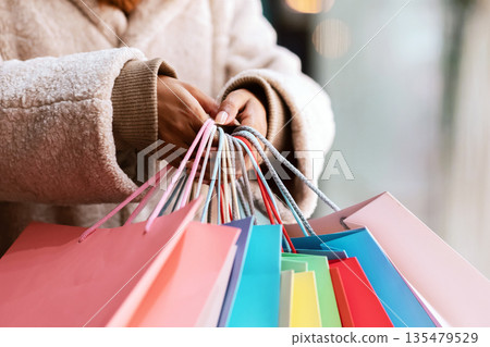 Time For Shopping Concept. Closeup of unrecognizable black female customer holding many colorful bags, walking outside near mall. African american woman carrying purchases and gifts. Retail And Sale 135479529