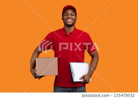 Parcel Receiving. Portrait Of Smiling African American Bearded Delivery Man Holding Clipboard And Cardboard Box, Nice Guy Delivering Goods And Food, Standing Over Orange Yellow Studio Background Parcel Receiving. Portrait Of Smiling African American Bearded Delivery Man Holding Clipboard And Cardboard Box, Nice Guy Delivering Goods And Food, Standing Over Orange Yellow Studio Background 135479532