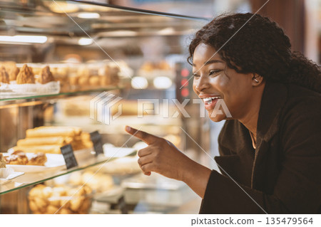 Delicious dessert in store or candy shop and discounts for sweets. Focus on smiling young african american woman points her finger at cake in showcase and want to buy, close up, copy space 135479564