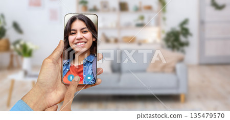 A person is having a friendly video call on a smartphone, enjoying the conversation with smiling Arab woman. The cozy home environment features a sofa and decorative elements in the background. A person is having a friendly video call on a smartphone, enjoying the conversation with smiling Arab woman. The cozy home environment features a sofa and decorative elements in the background. 135479570