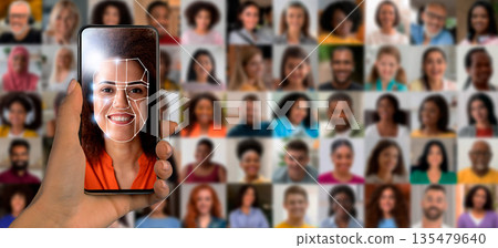 A hand holds a smartphone displaying facial recognition software. The screen shows a woman's face outlined for identification. A hand holds a smartphone displaying facial recognition software. The screen shows a woman's face outlined for identification. 135479640