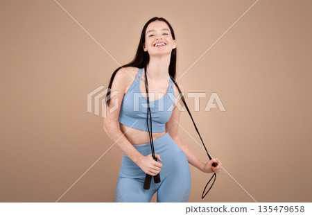 Fitness Concept. Portrait Of Cheerful Sporty Woman With Vitiligo Disorder Holding Jump Rope, Smiling At Camera, Fit Young Lady In Sportswear Posing Over Beige Studio Background, Copy Space 135479658