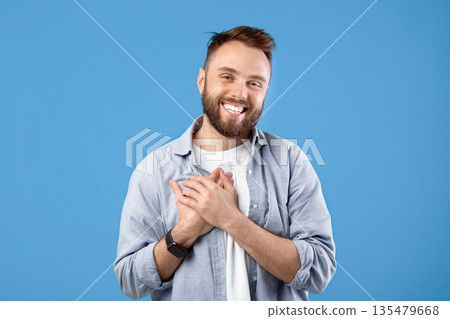 Cordial millennial guy holding his hand on chest, expressing gratitude and positive emotions on blue studio background. Pleased young man keeping palm on heart, feeling hope and love 135479668