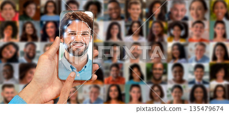 A person scans their face using a smartphone screen, showcasing advanced identification technology. The background features a collage of various faces, emphasizing modern identification systems. A person scans their face using a smartphone screen, showcasing advanced identification technology. The background features a collage of various faces, emphasizing modern identification systems. 135479674