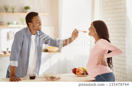 Positive black guy feeding yummy healthy meal to his pregnant wife in kitchen, panorama. Lovely African American expectant couple having breakfast together at home. Balanced pregnancy diet concept Positive black guy feeding yummy healthy meal to his pregnant wife in kitchen, panorama. Lovely African American expectant couple having breakfast together at home. Balanced pregnancy diet concept 135479744