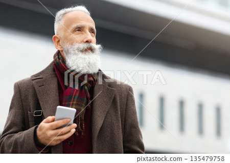 Senior grey-haired businessman using smartphone on the street, checking his agenda, looking at copy space. Bearded aged man using mobile phone, websurfing or chatting with colleagues, having break Senior grey-haired businessman using smartphone on the street, checking his agenda, looking at copy space. Bearded aged man using mobile phone, websurfing or chatting with colleagues, having break 135479758