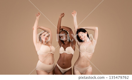 Love Your Body. Happy Three Women With Different Shapes And Appearance Posing Over Beige Studio Background, Positive Beautiful Multi-Ethnic Ladies In Underwear Enjoying Themselves, Copy Space 135479762