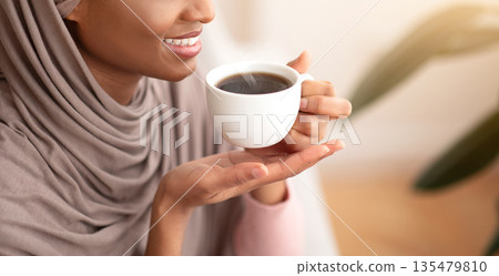 Happy morning. Happy Muslim woman in traditional hijab drinking strong black coffee at home. Smiling young lady having hot aromatic beverage, relaxing during her break 135479810