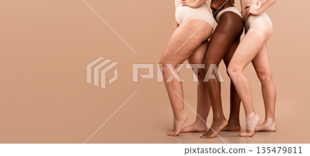 Cropped Image Of Three Multiethnic Women Posing In Underwear Over Beige Background, Bottom Part Of Multicultural Group Of Unrecognizable Ladies Wearing Lingerie Standing Together In Studio, Copy Space 135479811