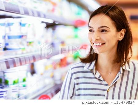 Retail Concept. Closeup Portrait Of Smiling Young Woman Standing Near The Shelves In Grocery Store. Cheerful Female Customer Buying Essentials In Super Market, Looking At Aisle With Dairy Products Retail Concept. Closeup Portrait Of Smiling Young Woman Standing Near The Shelves In Grocery Store. Cheerful Female Customer Buying Essentials In Super Market, Looking At Aisle With Dairy Products 135479824