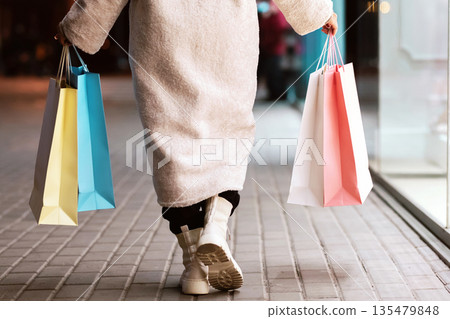 Satisfied Customer. Closeup of unrecognizable black female customer walking away and holding colorful shopping bags near mall center in the evening, rear view from the back. Retail And Purchase Satisfied Customer. Closeup of unrecognizable black female customer walking away and holding colorful shopping bags near mall center in the evening, rear view from the back. Retail And Purchase 135479848