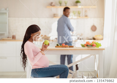 Beautiful pregnant woman with apple and her loving boyfriend cooking balanced meal at kitchen, copy space. Millennial expectant couple eating healthy at home. Perfect pregnancy diet concept Beautiful pregnant woman with apple and her loving boyfriend cooking balanced meal at kitchen, copy space. Millennial expectant couple eating healthy at home. Perfect pregnancy diet concept 135479862