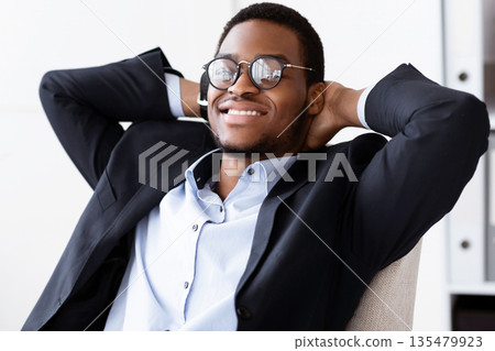 Joyful black businessman in suit reclining on chair and smiling in his modern office, having break after successful working day, achieved goals or had important business meeting, closeup Joyful black businessman in suit reclining on chair and smiling in his modern office, having break after successful working day, achieved goals or had important business meeting, closeup 135479923